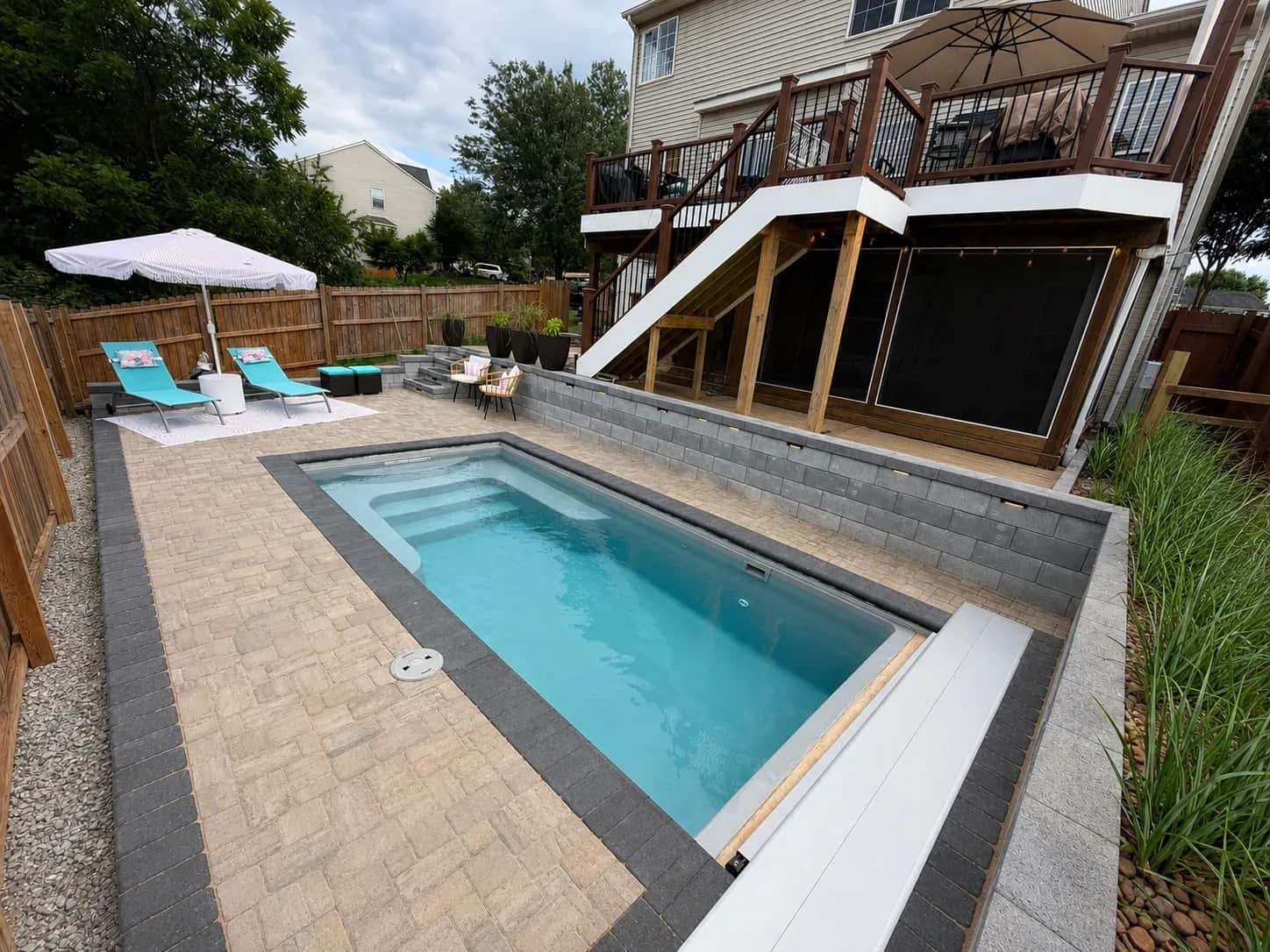 Finished fiberglass pool with paver patio, retaining wall, privacy fence, and deck stairs in Culpeper VA
