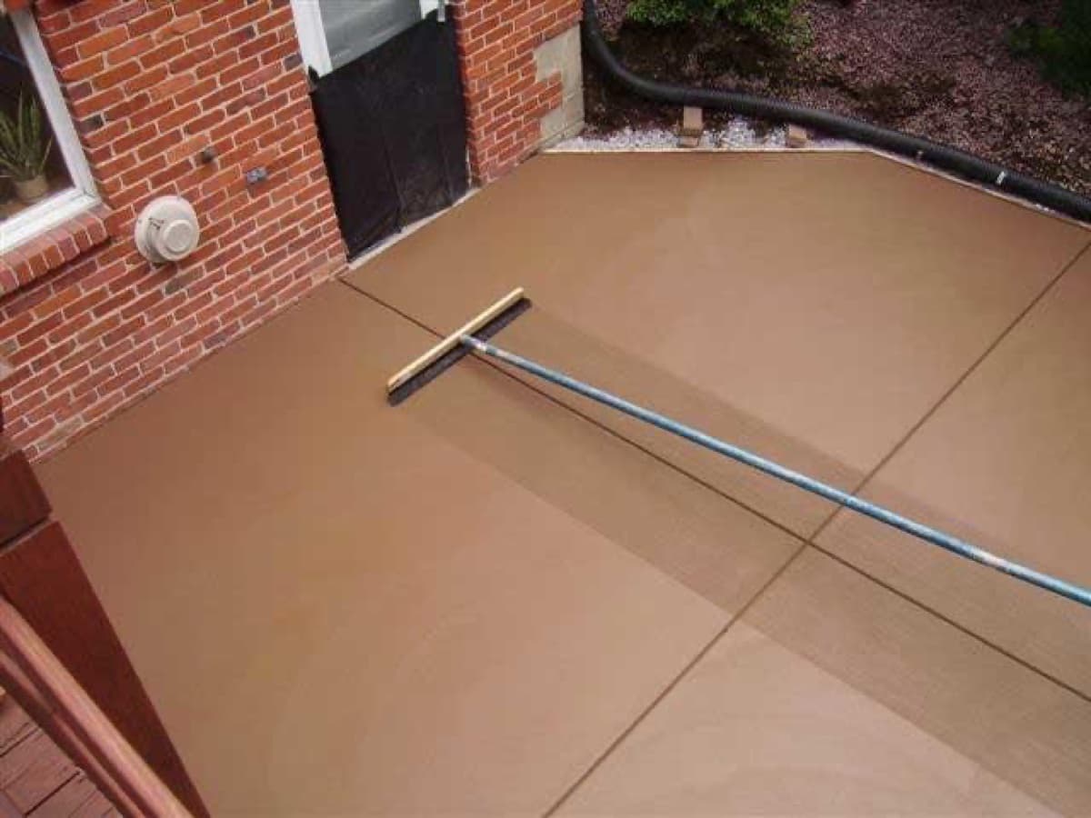 Color-infused concrete patio being broom finished beside a brick home