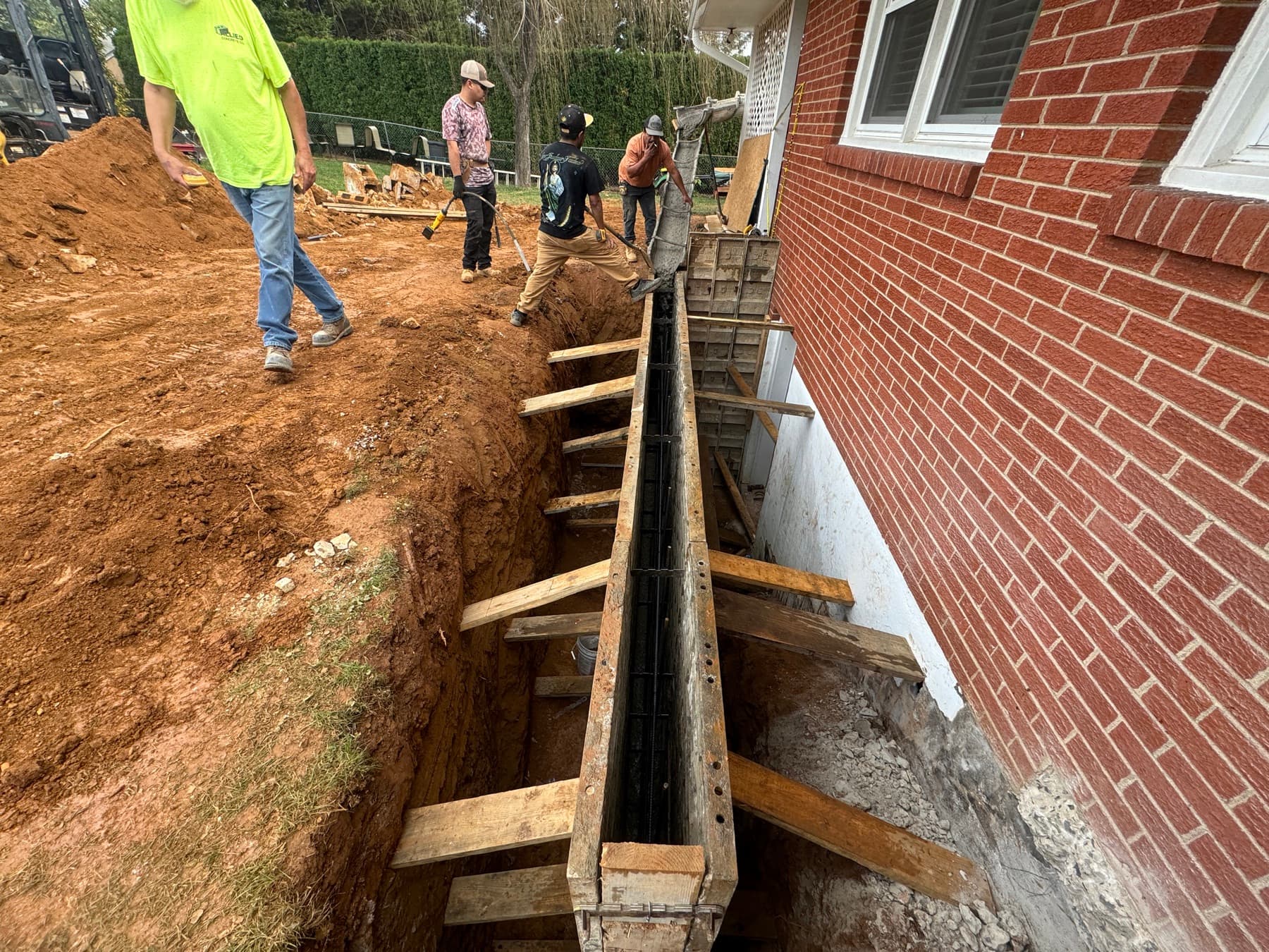 Basement egress entrance excavation with stairwell formwork beside a brick home